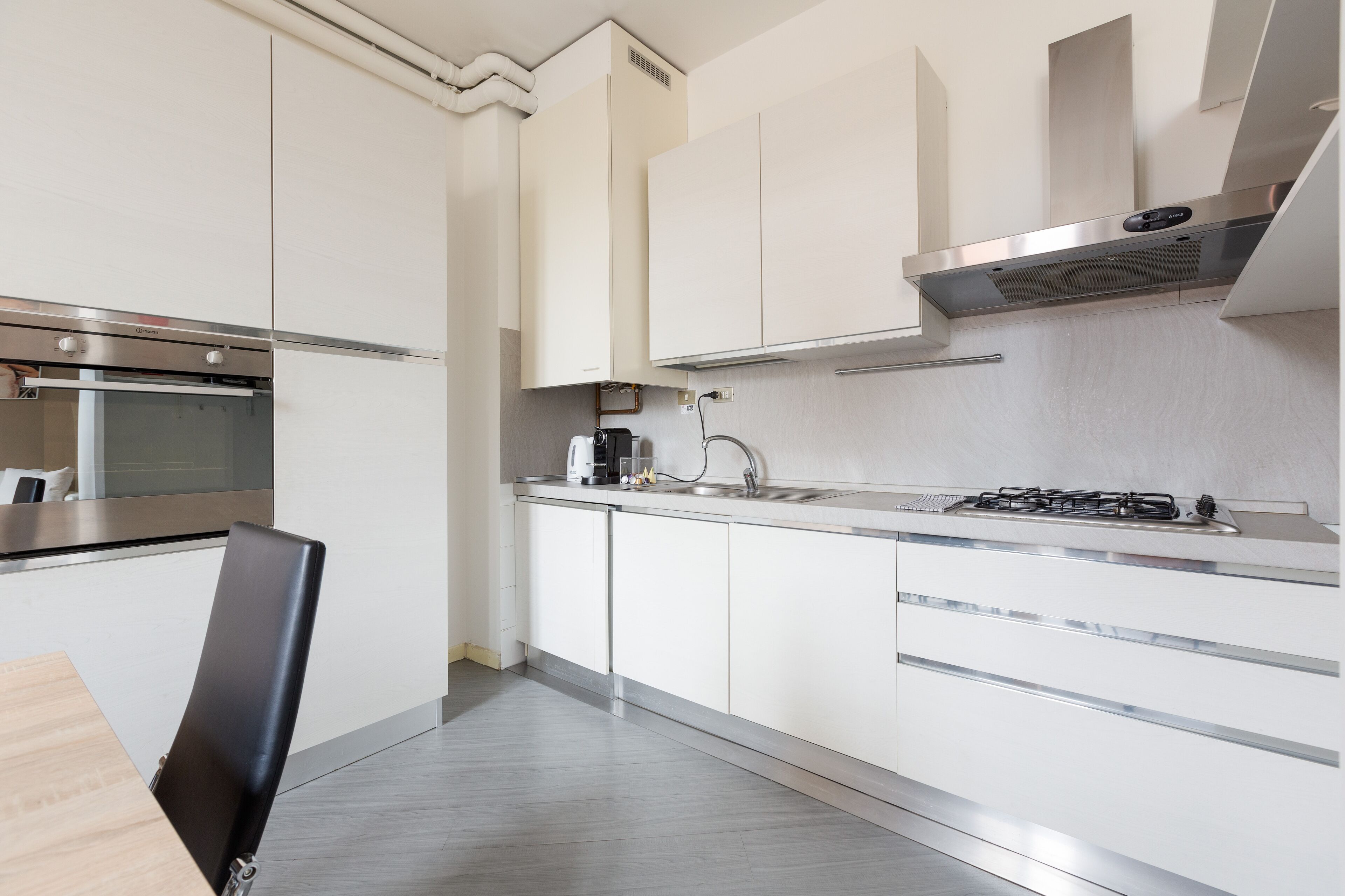 A modern kitchen with white cabinetry, stainless steel appliances, and a wooden dining table.