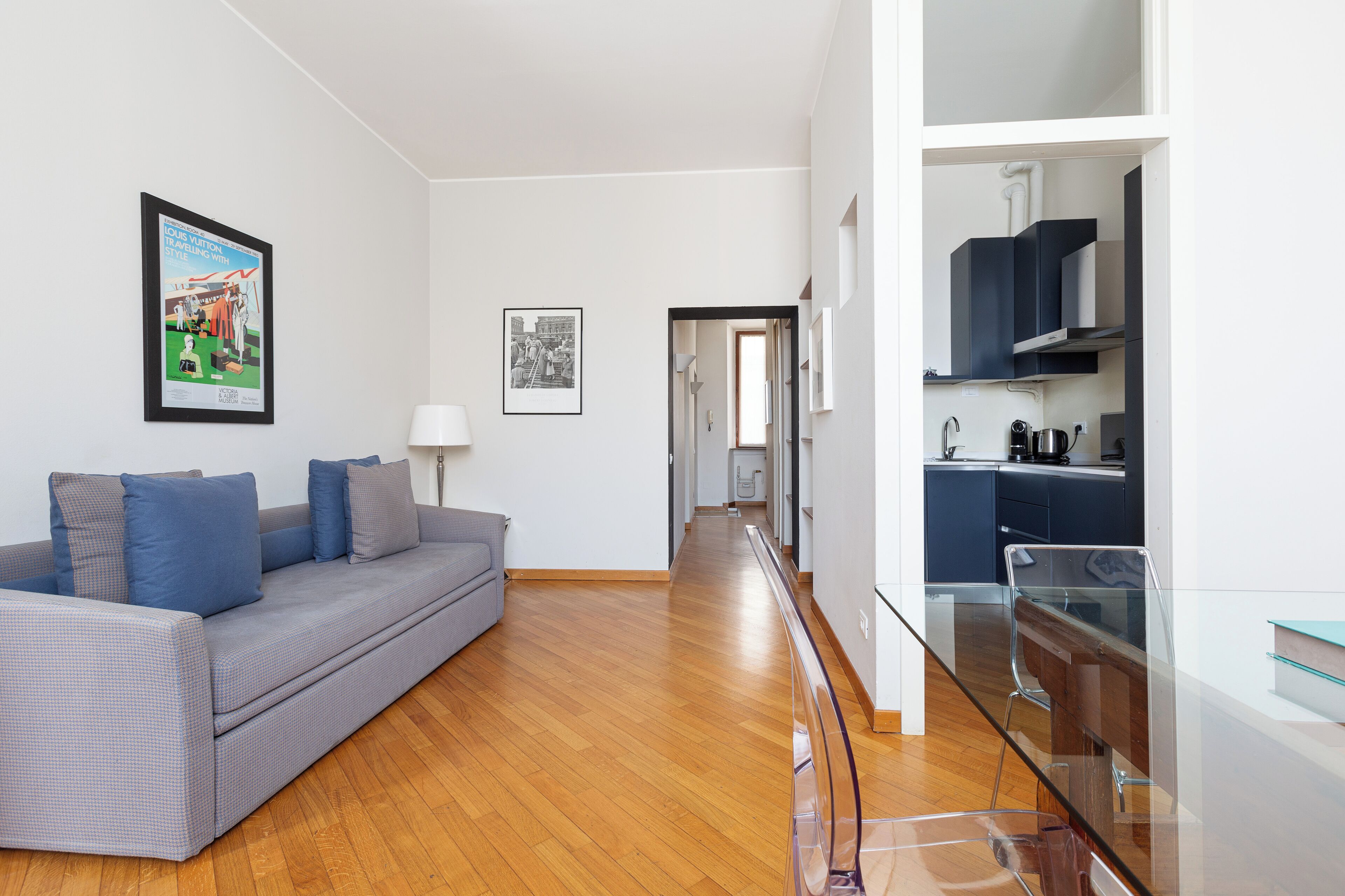 Un soggiorno moderno con un divano grigio, un tavolo da pranzo in vetro e una zona cucina con mobili scuri.