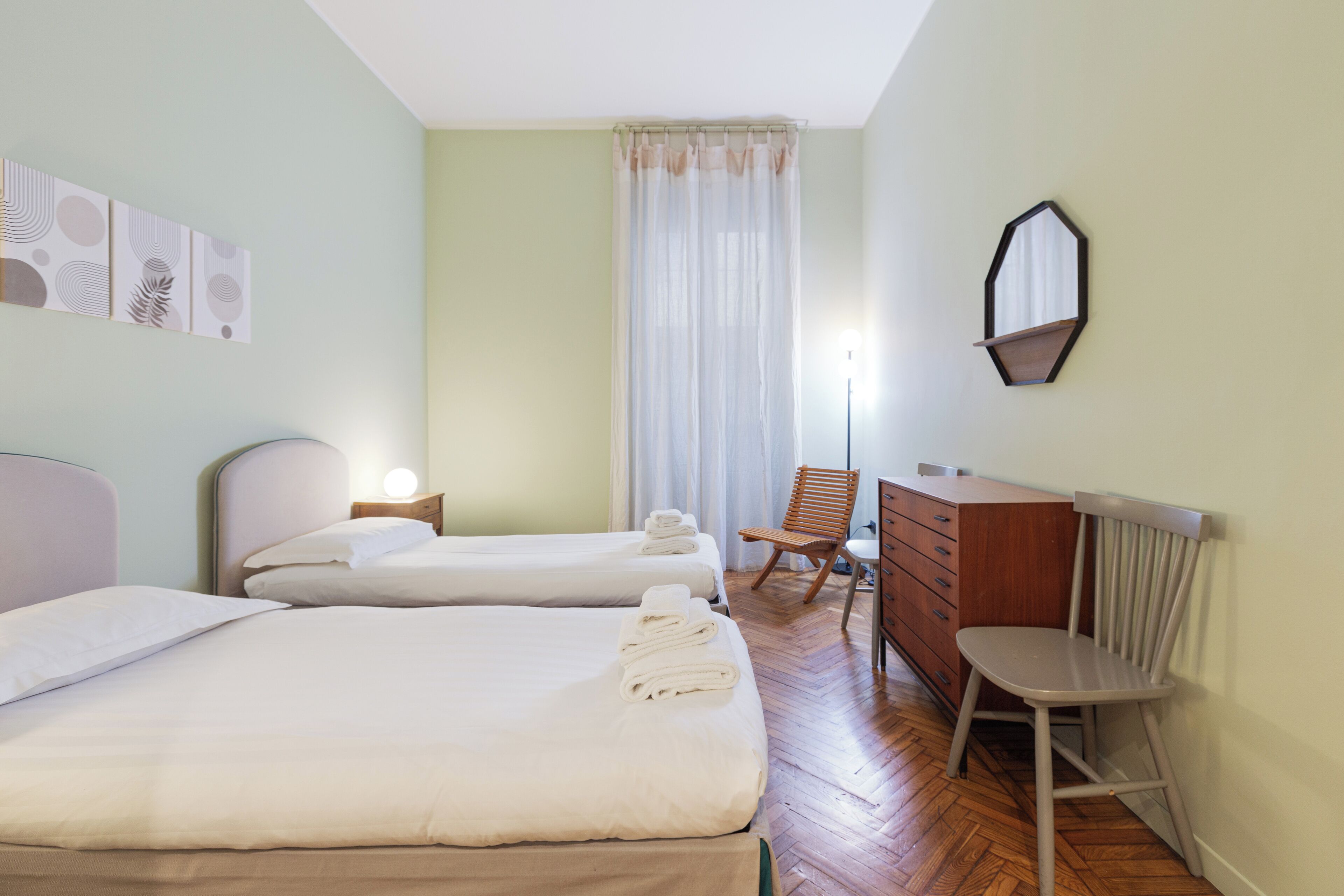 A hotel room with two beds, a wooden dresser, a chair, and a mirror on the wall.