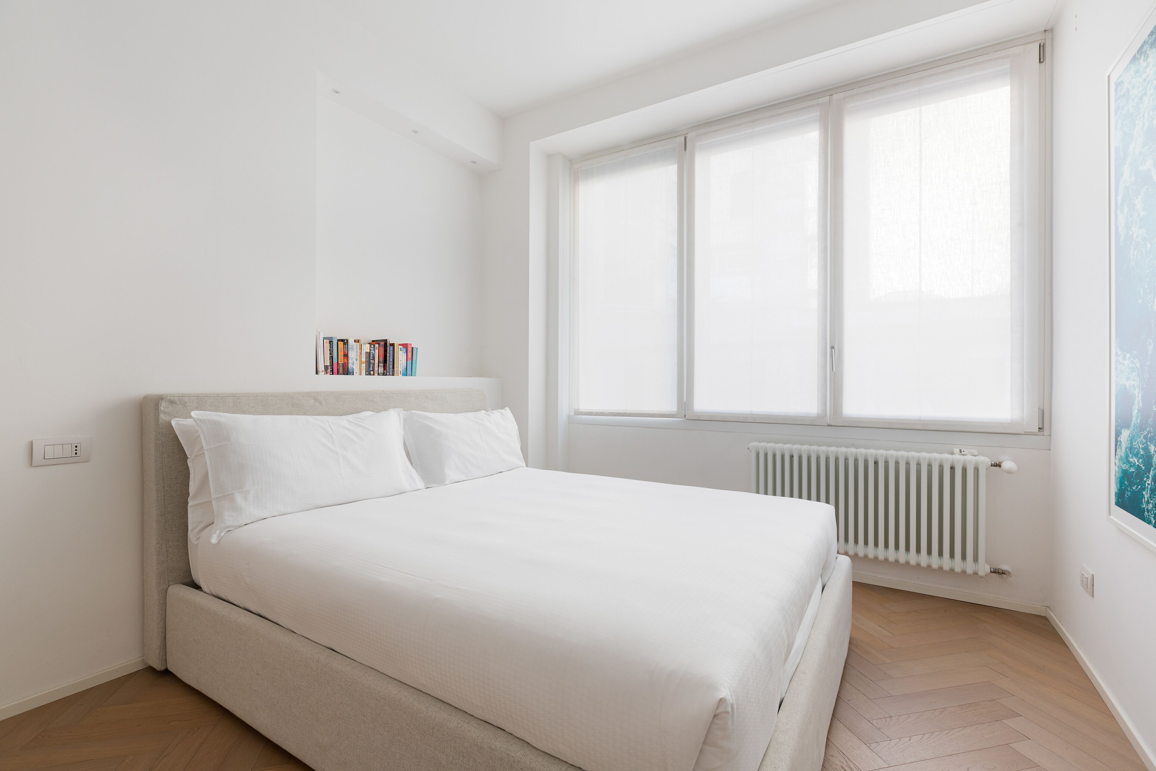 A bedroom with a bed, a radiator, a window, and a bookshelf.