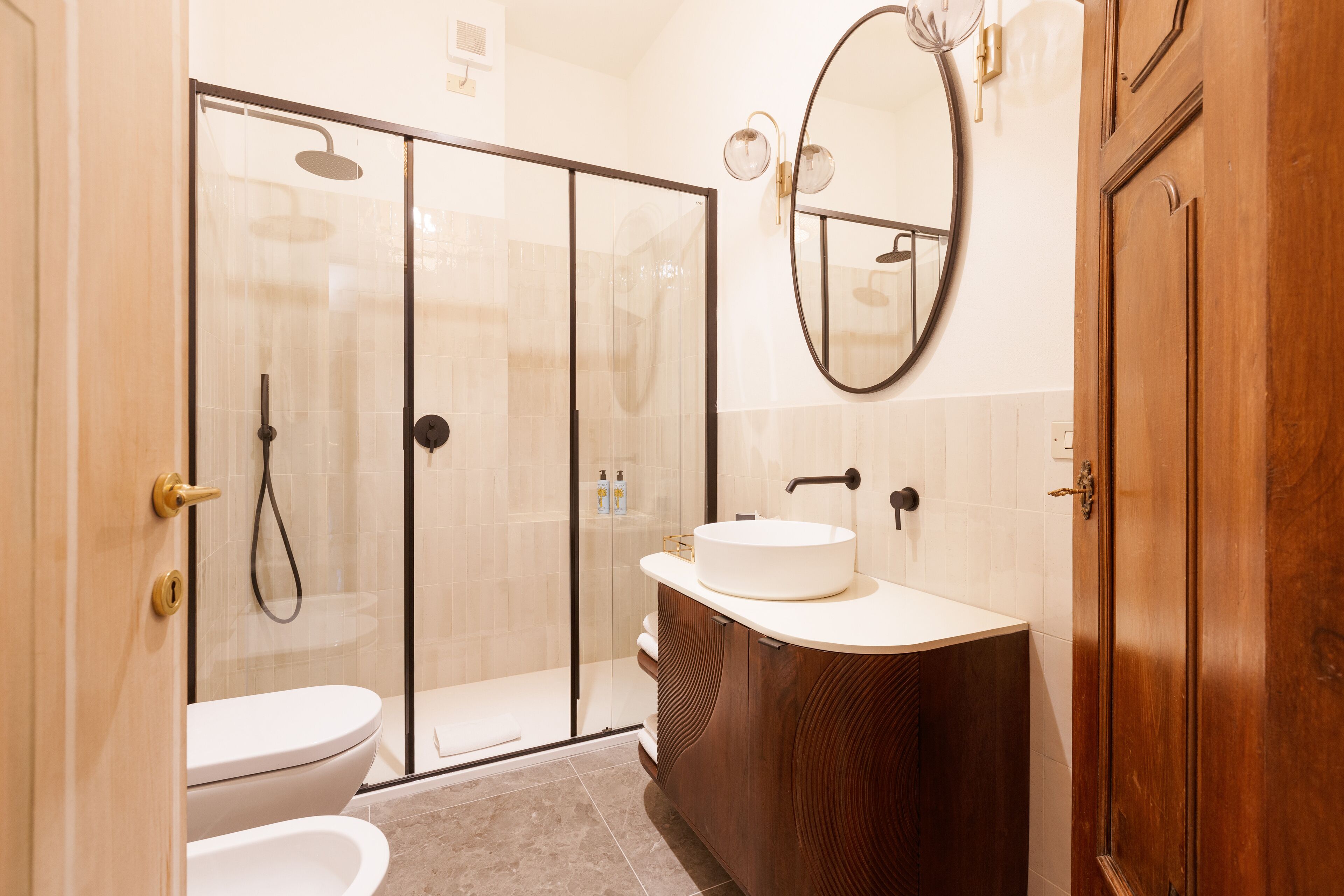 Un baño moderno con ducha envuelta en vidrio, un lavabo blanco y un mueble de tocador de madera.