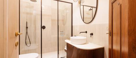 Un baño moderno con ducha envuelta en vidrio, un lavabo blanco y un mueble de tocador de madera.