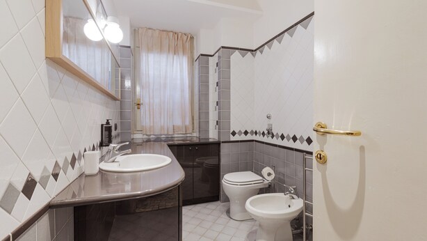 A bathroom with a sink, toilet, bidet, and a mirror. - Brera Apartments in Garibaldi (Milan)