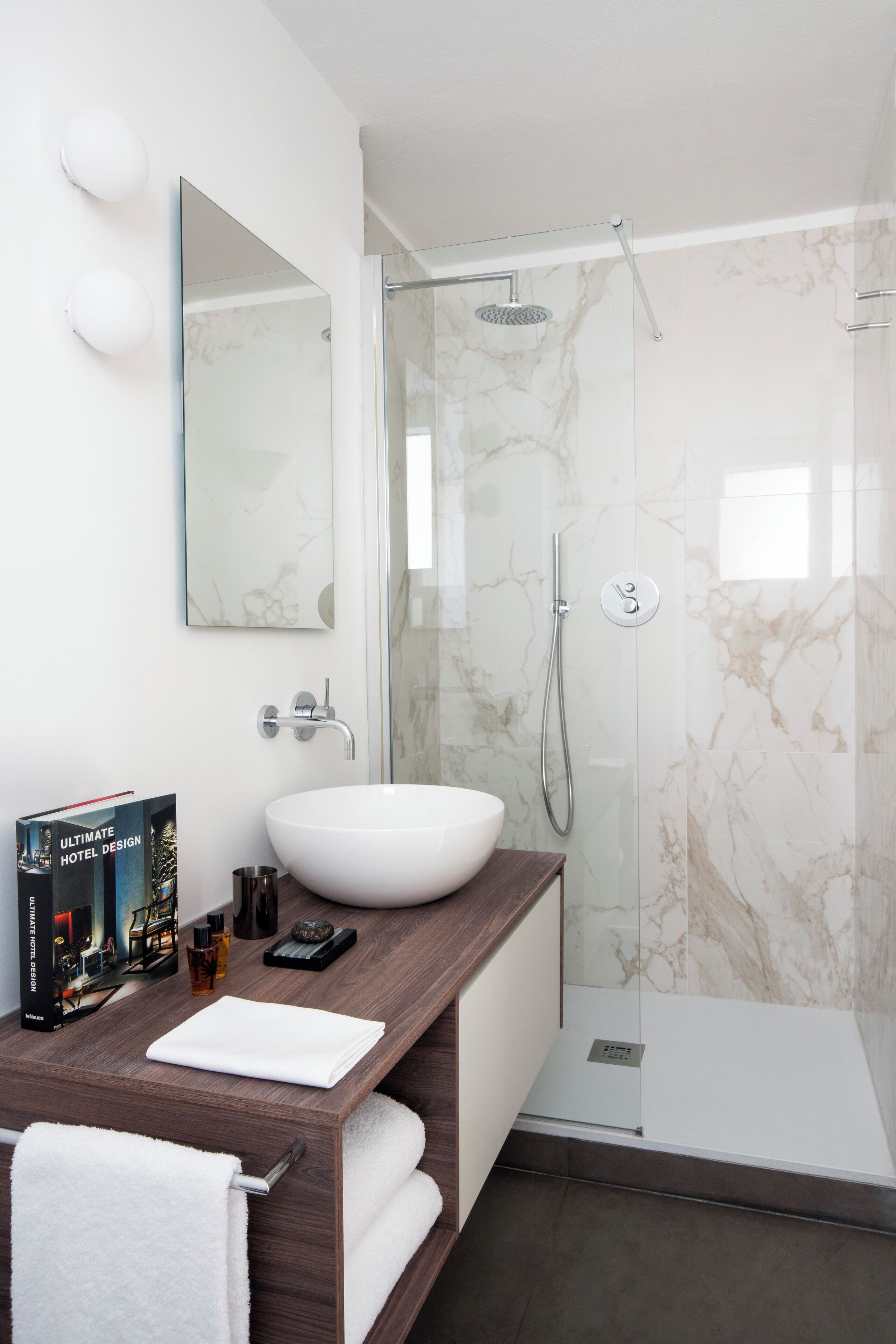 A modern bathroom with a white sink, a glass shower enclosure, and a marble backsplash.
