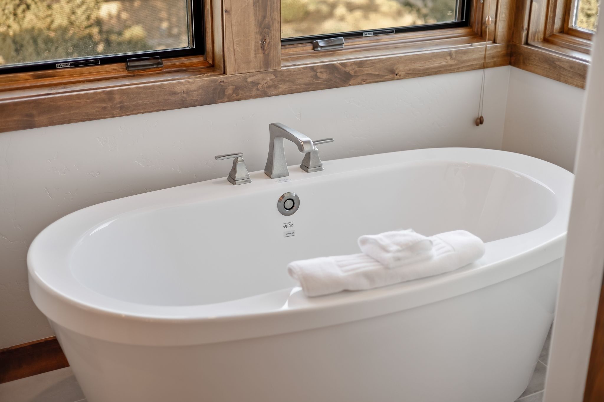 Una vasca da bagno bianca con un asciugamano, un rubinetto e una finestra sopra.