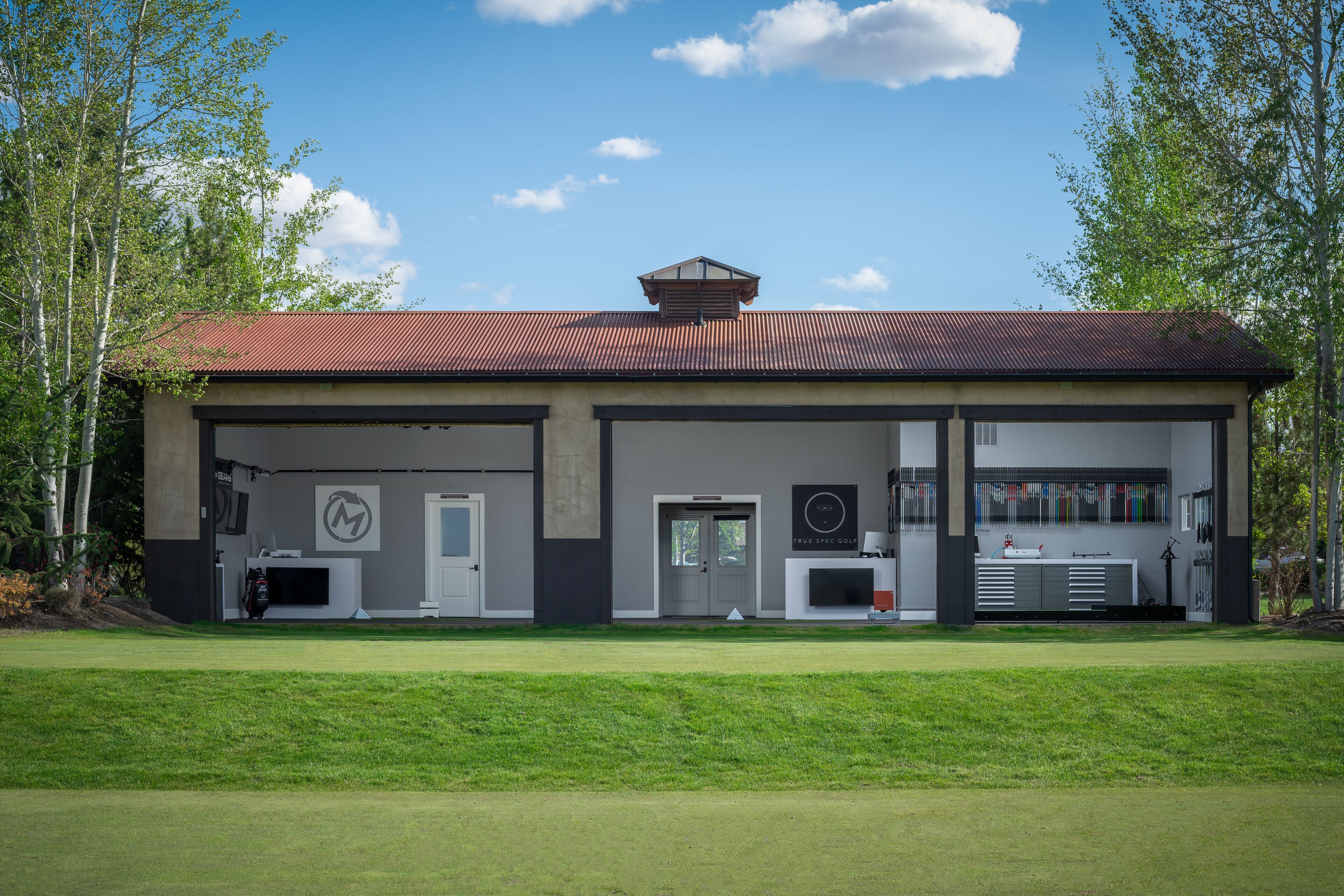 Een modern gebouw met een rood dak, een garagepoort en een bord waarop 'True Spec Golf' staat.