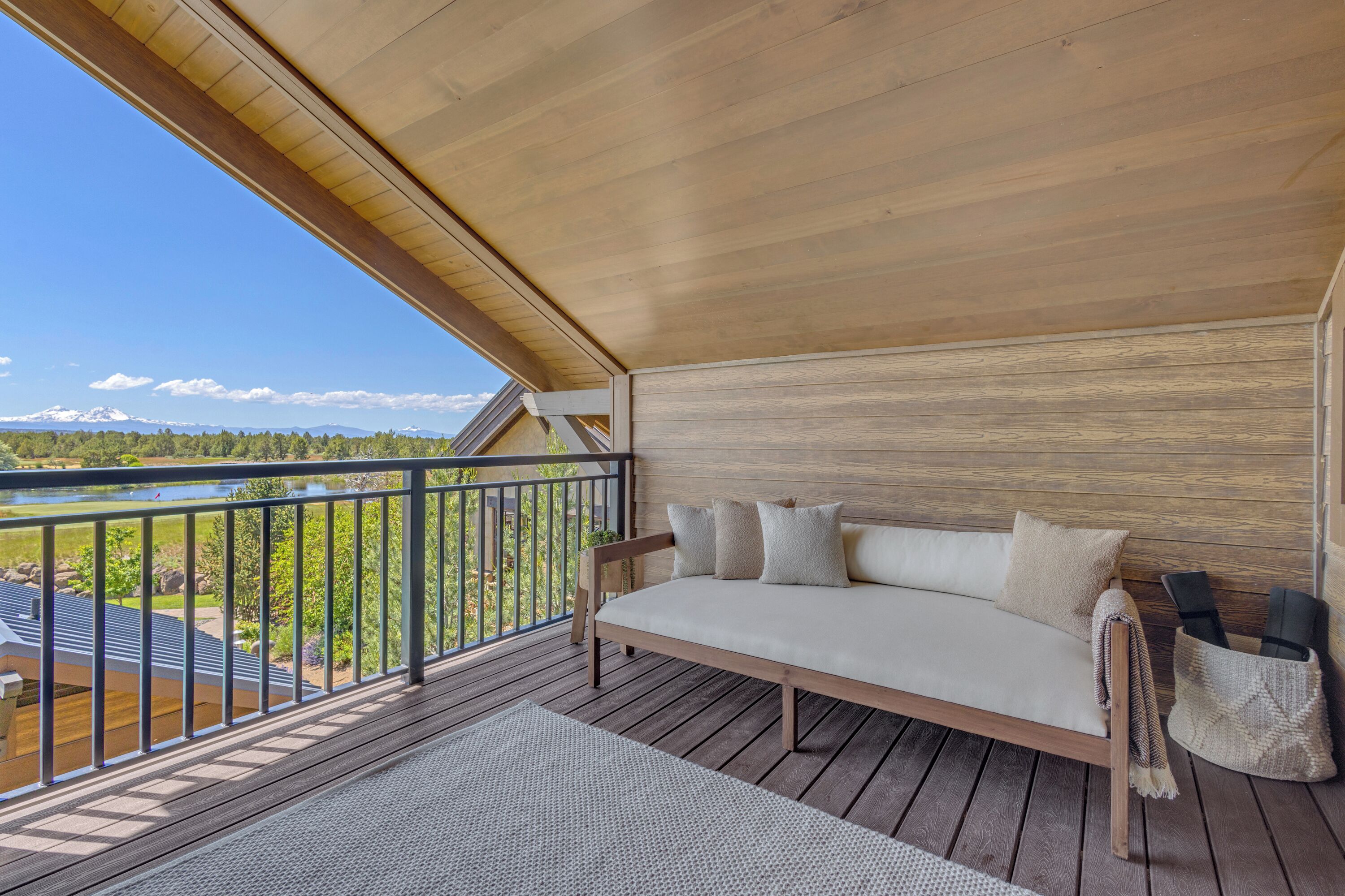 A wooden deck with a sofa and cushions, overlooking a lake and mountains.