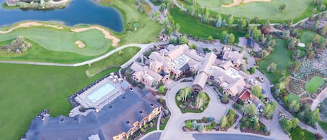 An aerial view of a golf course with a clubhouse, parking areas, and water bodies.