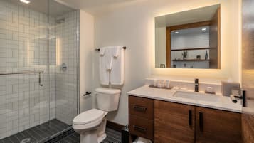 Une salle de bain moderne avec une douche à parois de verre, des toilettes blanches, un meuble-lavabo en bois avec un miroir et un évier.