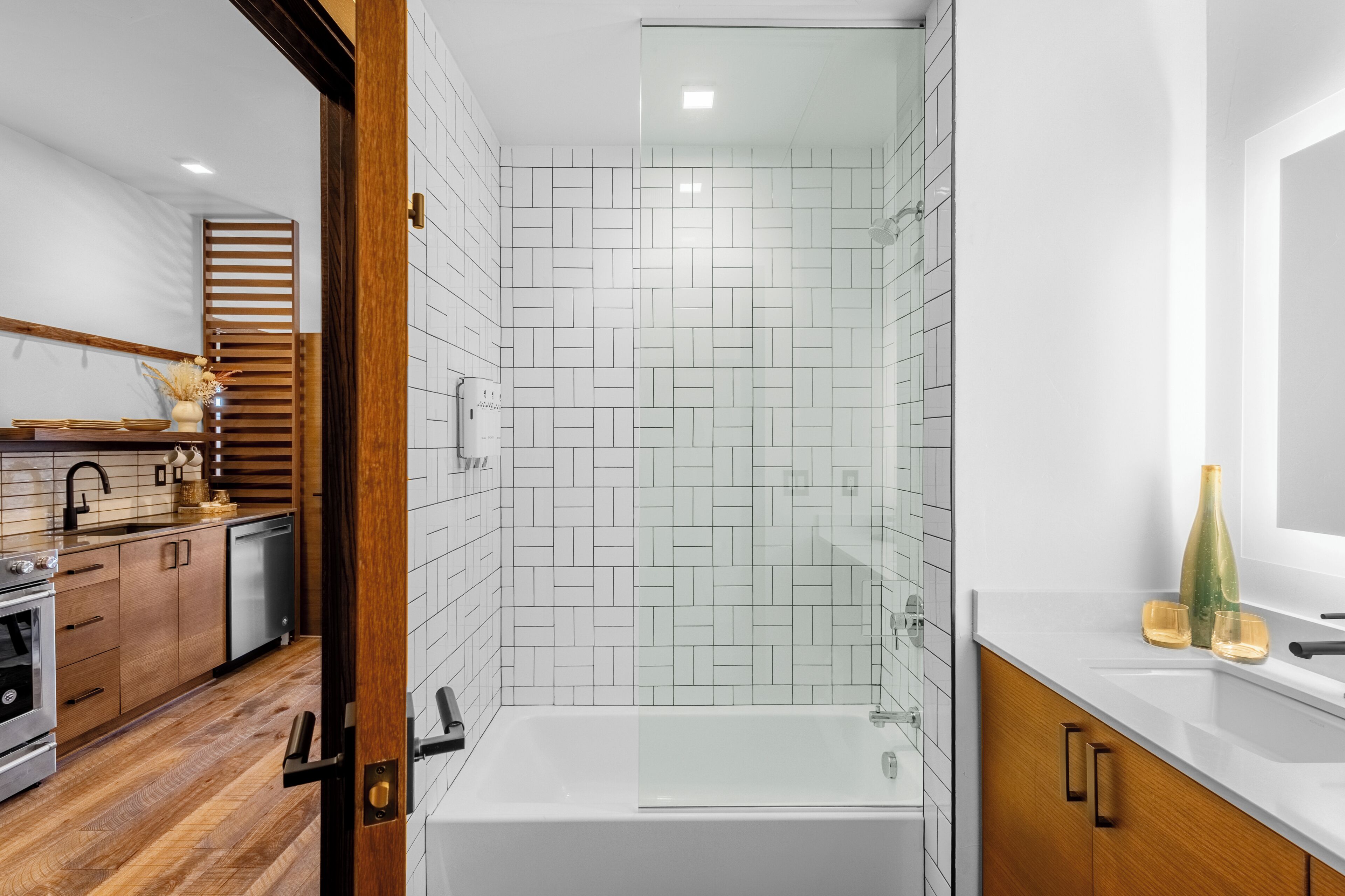 A modern bathroom with a glass-enclosed shower, a white bathtub, and a wooden vanity with a sink.