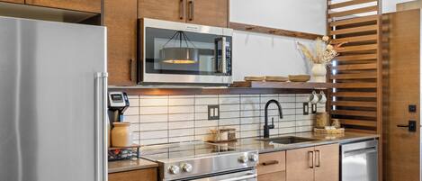 Una cocina moderna con electrodomésticos de acero inoxidable, armarios de madera y salpicadero de azulejos.