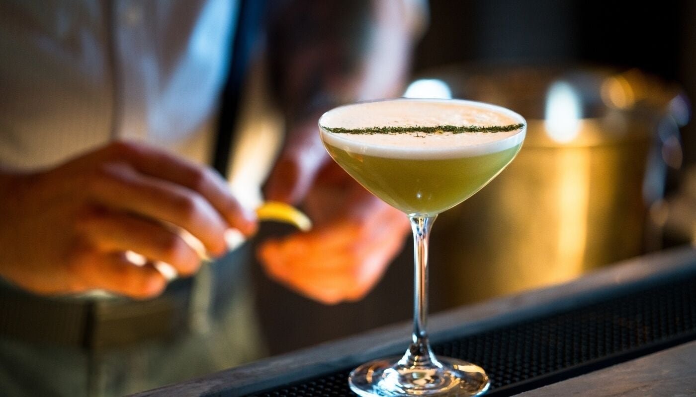 A cocktail in a martini glass with a garnish on the rim, placed on a bar counter.