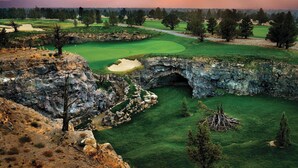 A golf course with a stone bridge, green fairways, and a mountainous backdrop. - Juniper Preserve (Bend)