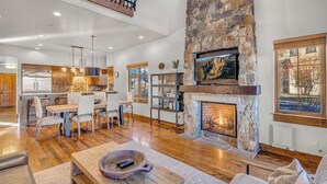 A spacious living area with a stone fireplace, wooden flooring, and a dining area with modern furniture. - Juniper Preserve (Bend)