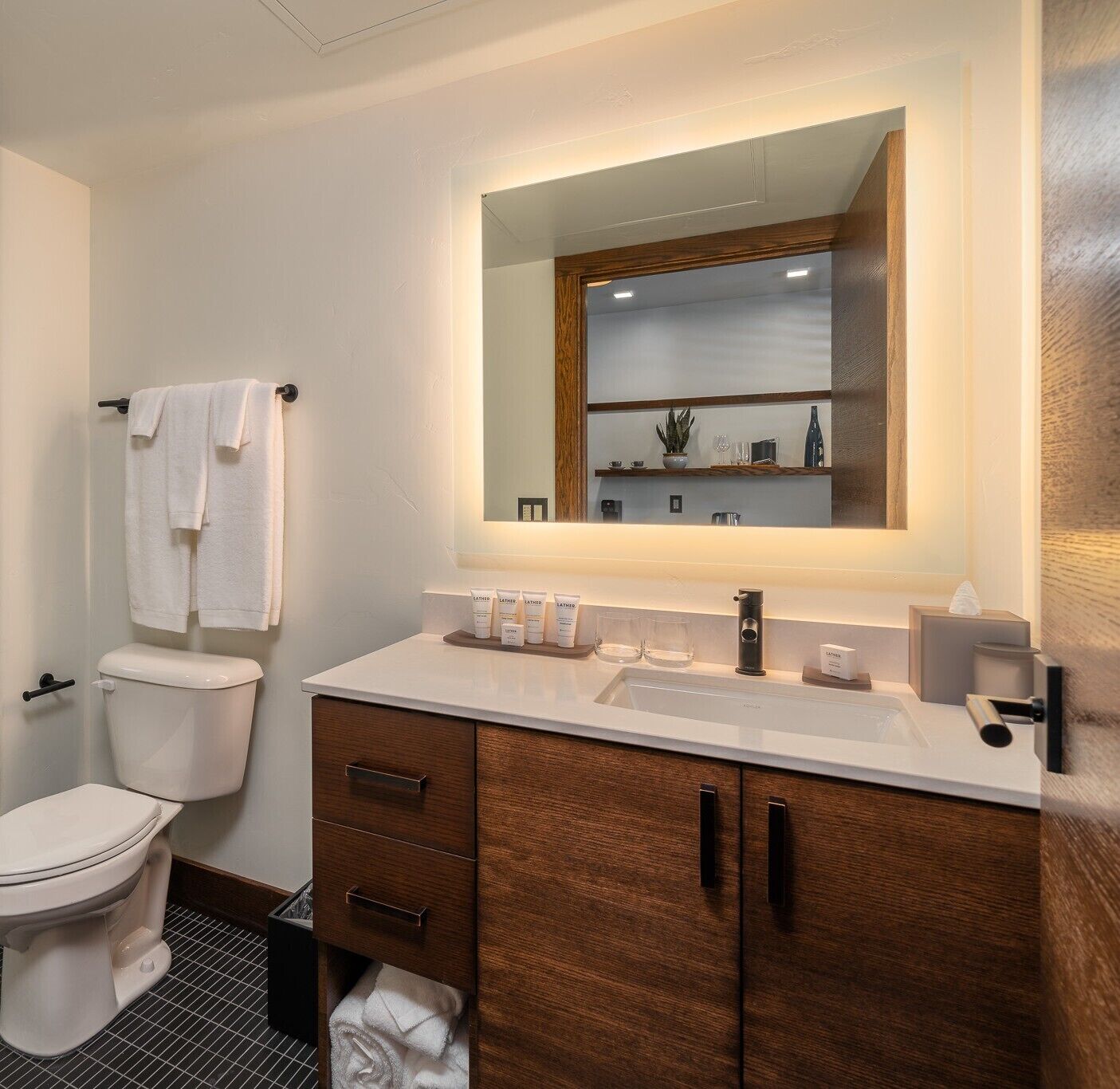 Un baño moderno con inodoro blanco, tocador de madera con espejo y lavabo.