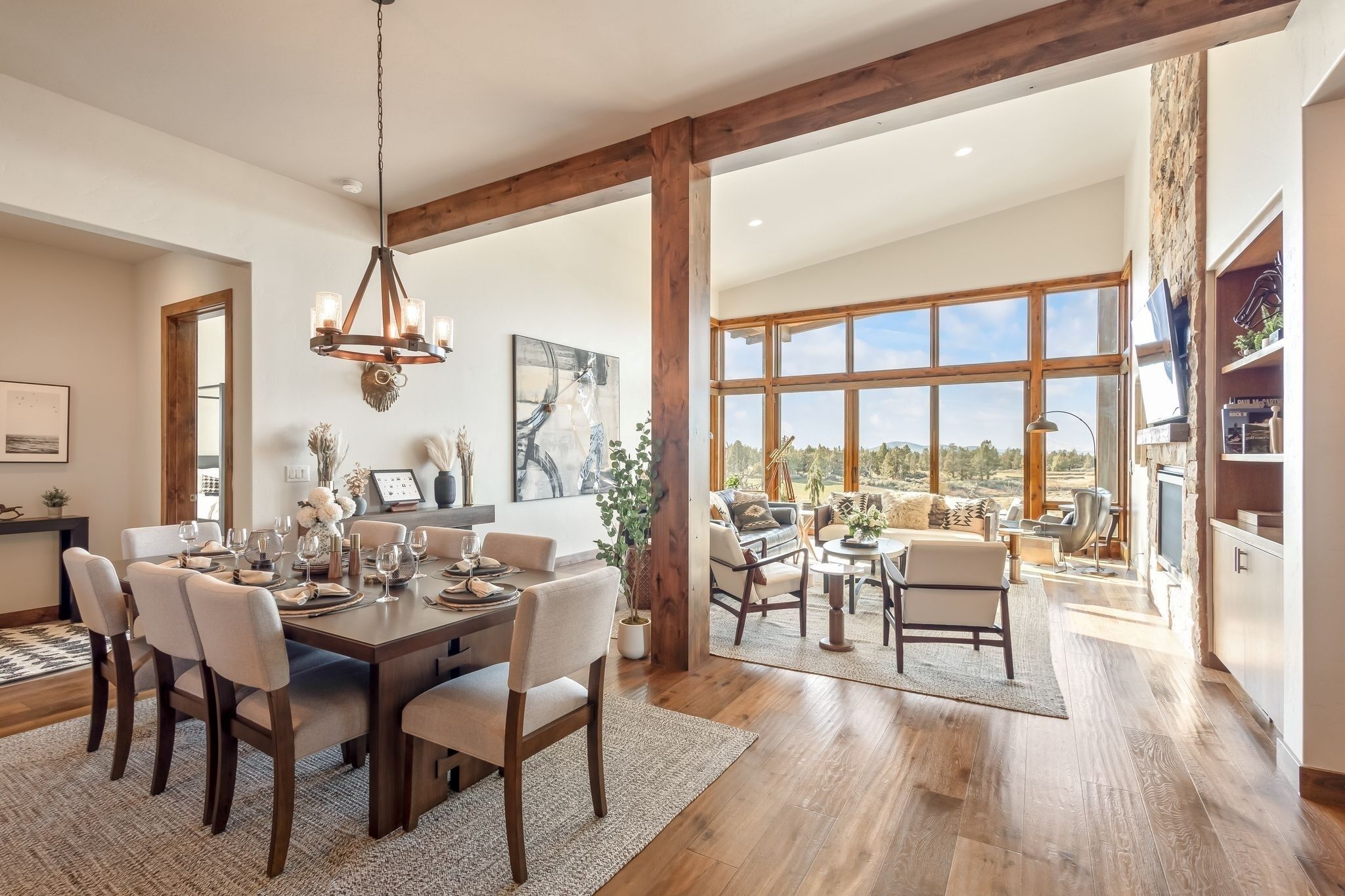 A spacious dining area with a wooden table set for six, flanked by large windows offering a view of the outdoors.
