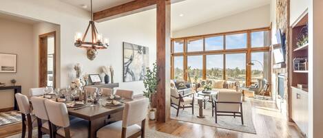A spacious dining area with a wooden table set for six, flanked by large windows offering a view of the outdoors.