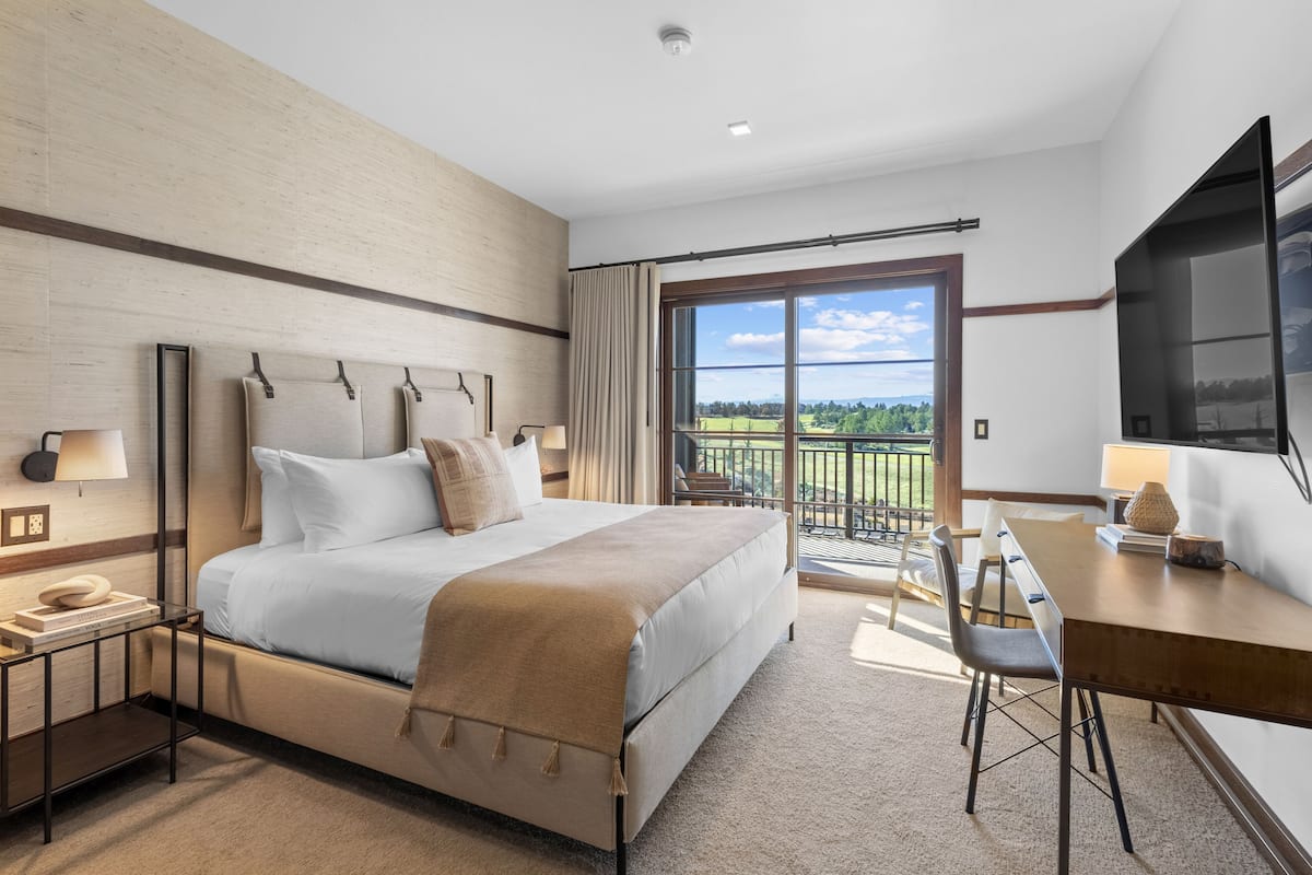 A hotel room with a bed, bedside tables, a desk, a chair, a TV, and a balcony with a view.
