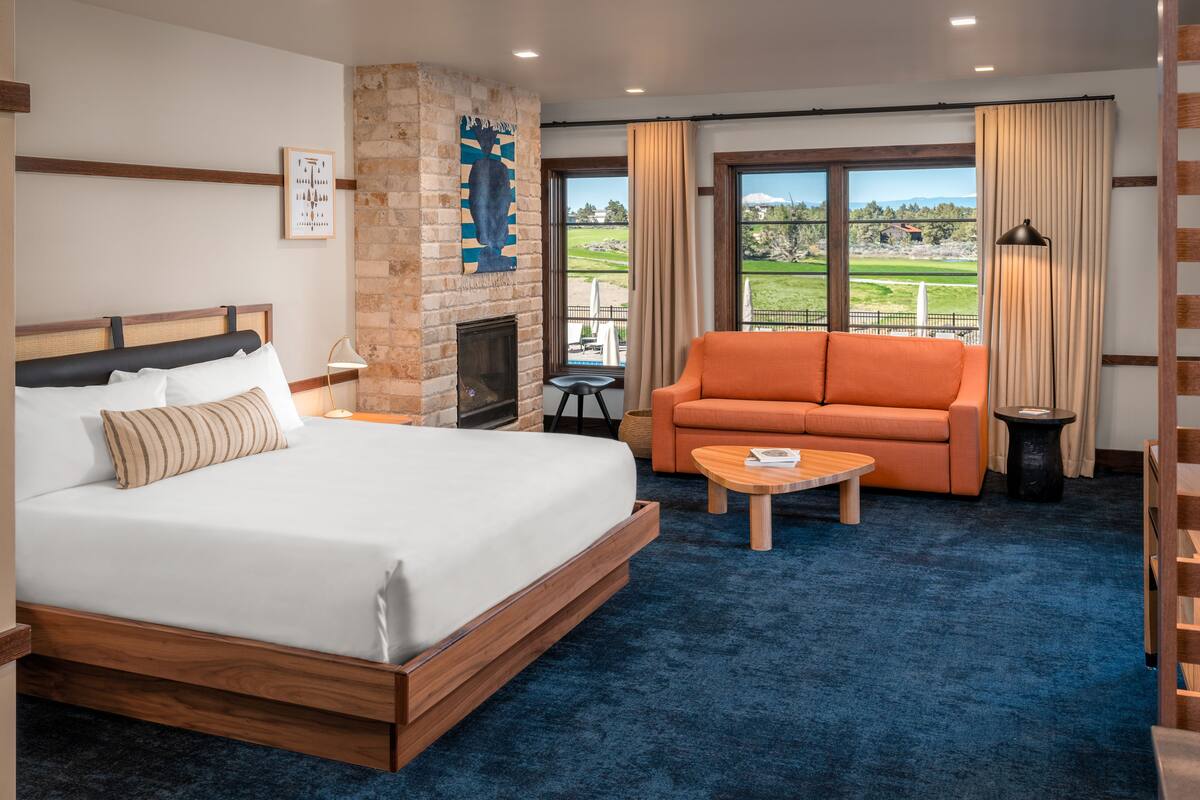 A hotel room with a large bed, an orange sofa, a small table, and a fireplace.