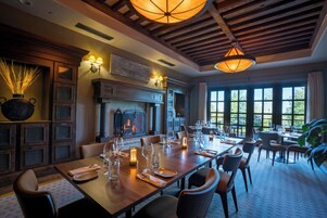 Un comedor con una larga mesa dispuesta para una comida, una chimenea y ventanas amplias.