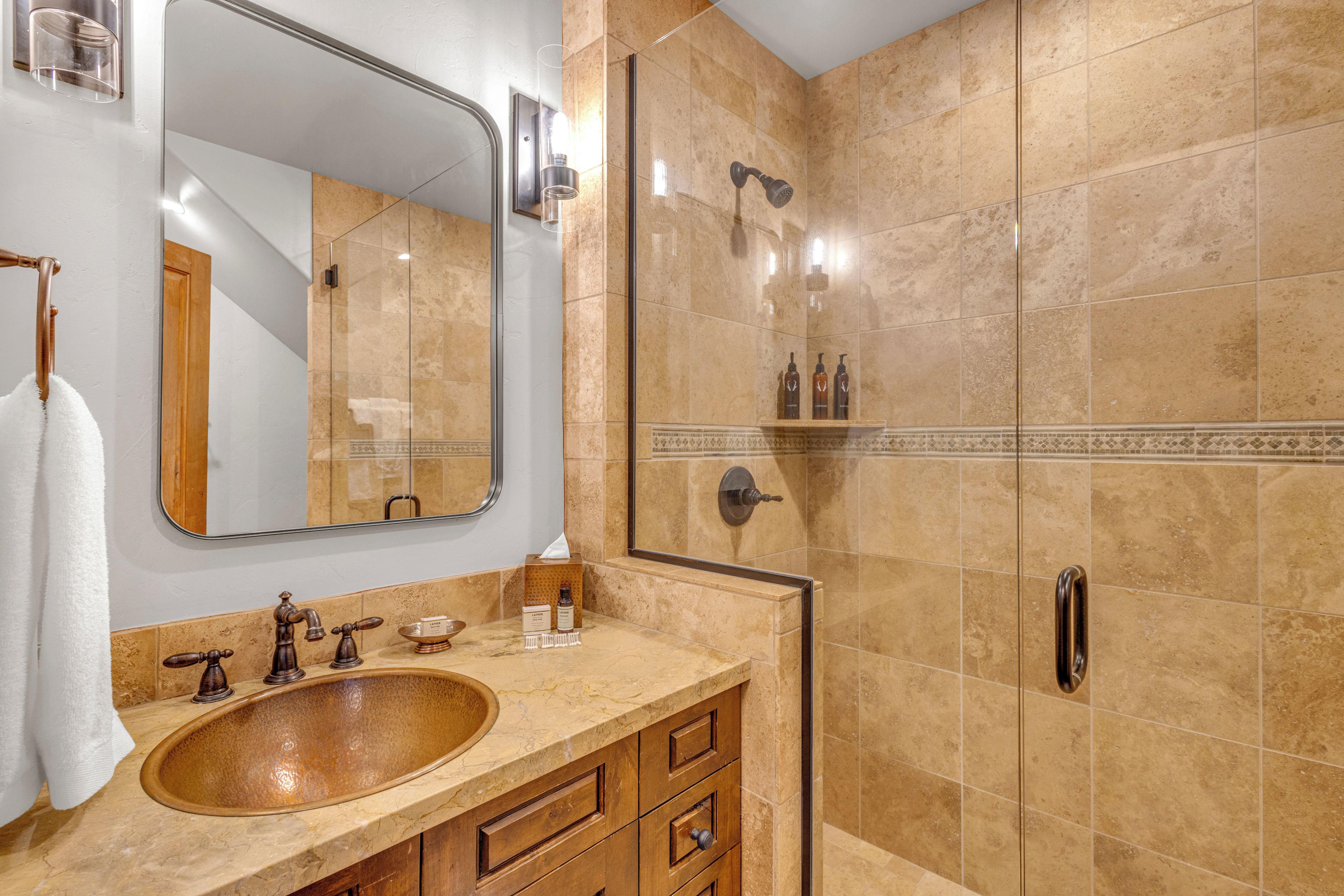 A bathroom with a large mirror, a wooden vanity, a sink, and a shower area.