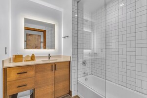 Un baño moderno con tocador de madera, un espejo y zona de ducha con paredes de vidrio.