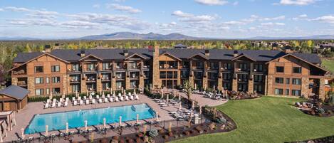 A multi-story hotel with a pool, outdoor seating, and a view of mountains.