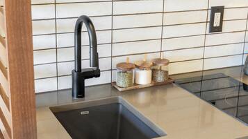 Una cocina con un grifo negro, un lavamanos y frascos de especias de madera sobre una encimera.