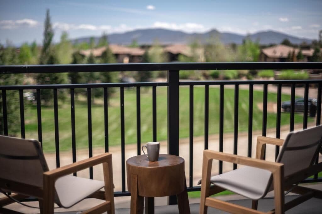 Un balcón con dos sillas de madera y una pequeña mesa redonda, con vistas a campos verdes y montañas al fondo.