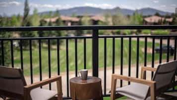 Un balcón con dos sillas de madera y una pequeña mesa redonda, con vistas a campos verdes y montañas al fondo.