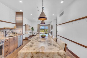 A modern kitchen with a marble countertop, wooden cabinetry, and a hanging pendant light.
