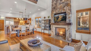 A spacious living area with a stone fireplace, wooden flooring, a dining area, and a kitchen with modern appliances. - Juniper Preserve (Bend)