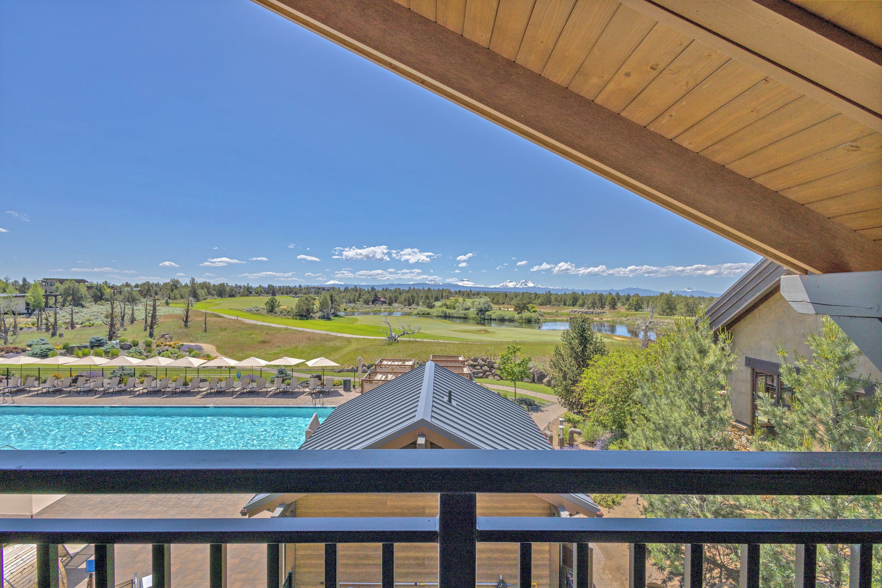 Une piscine avec des chaises longues et des parasols, une vue sur un terrain de golf et, au loin, une chaîne de montagnes.