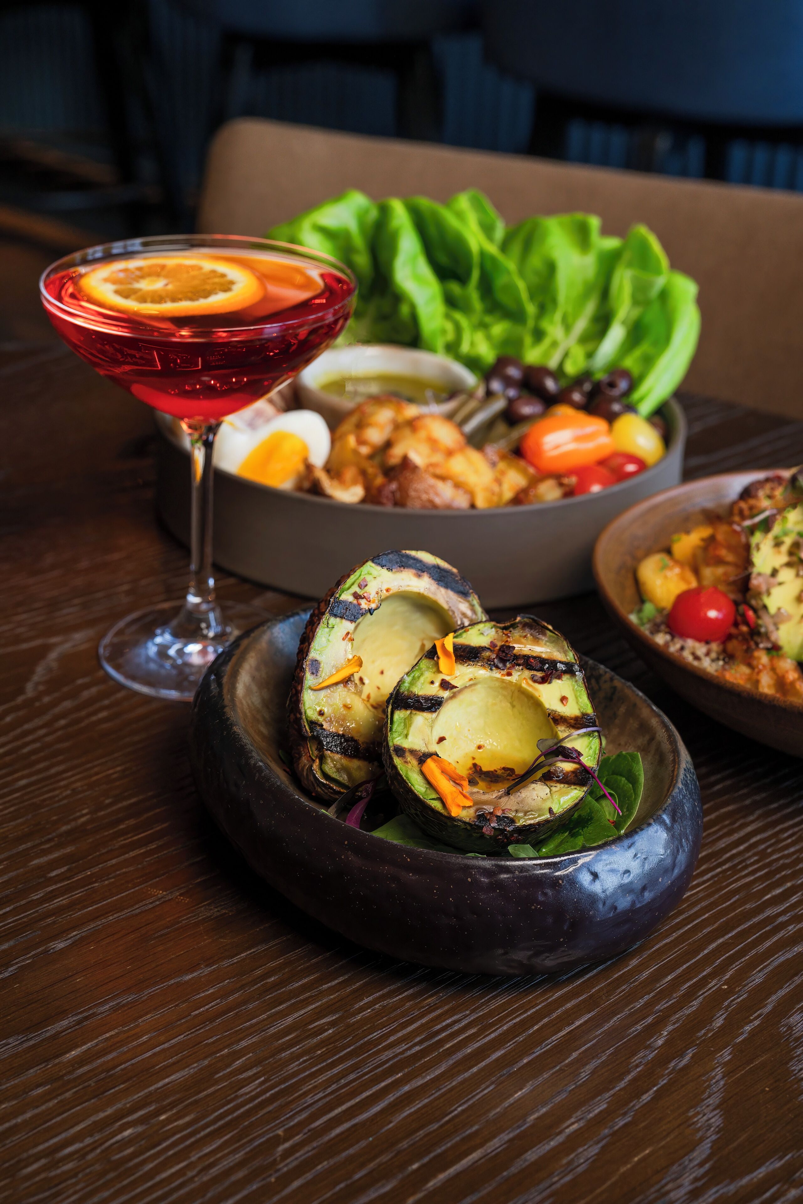 Ein Esstisch mit einer Salatschüssel, gegrilltem Gemüse und einem Martini-Glas.