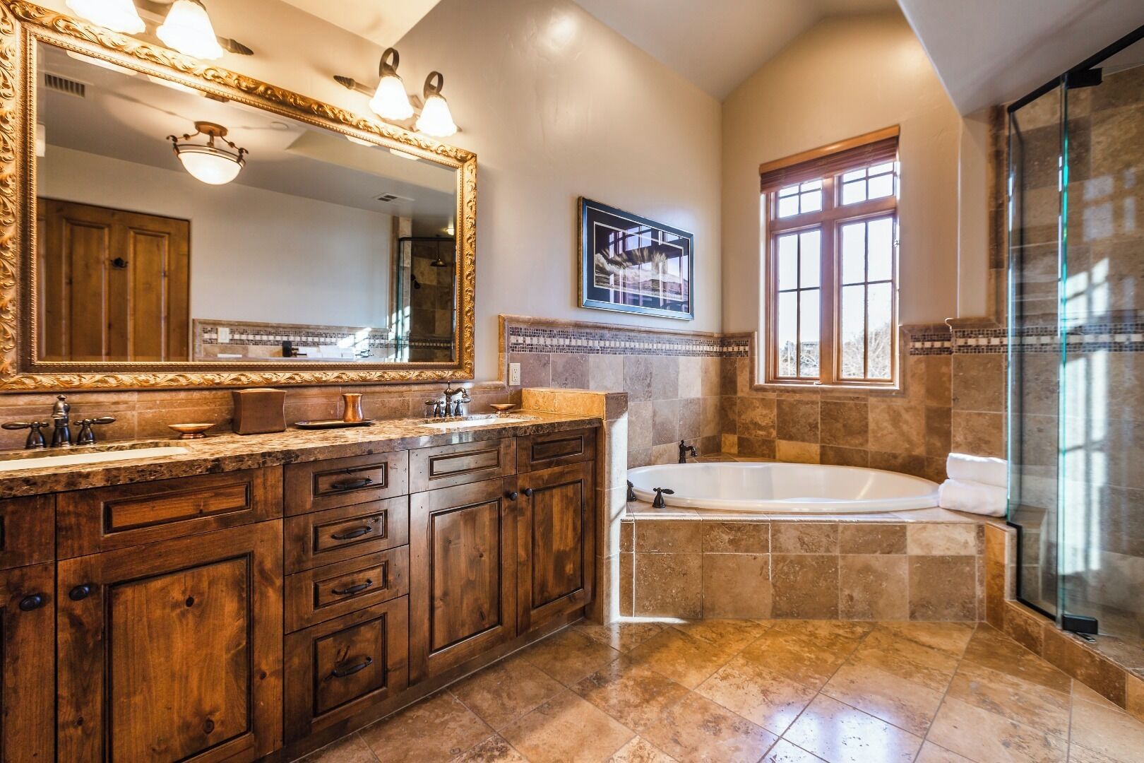 A bathroom with a wooden vanity, a large mirror, a bathtub, and a window.