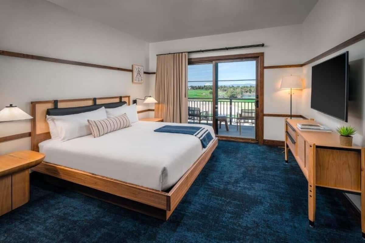 A hotel room with a large bed, a desk, a TV, and a balcony with a view.