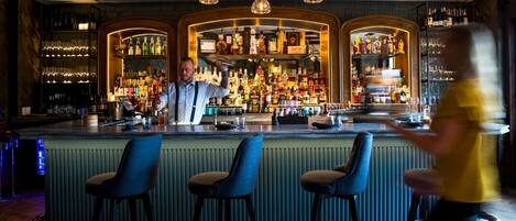 A bar area with a bartender, shelves of liquor, and bar stools.