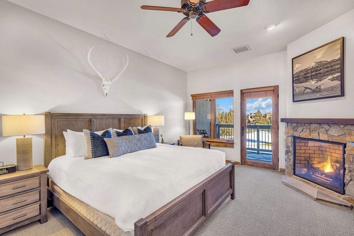 A spacious bedroom with a large bed, a ceiling fan, a fireplace, and a mounted deer head on the wall.