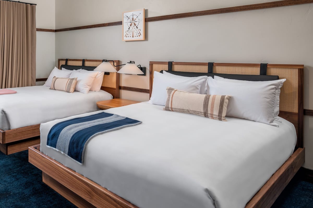 A hotel room with two beds, wooden headboards, white bedding, and a blue carpet.