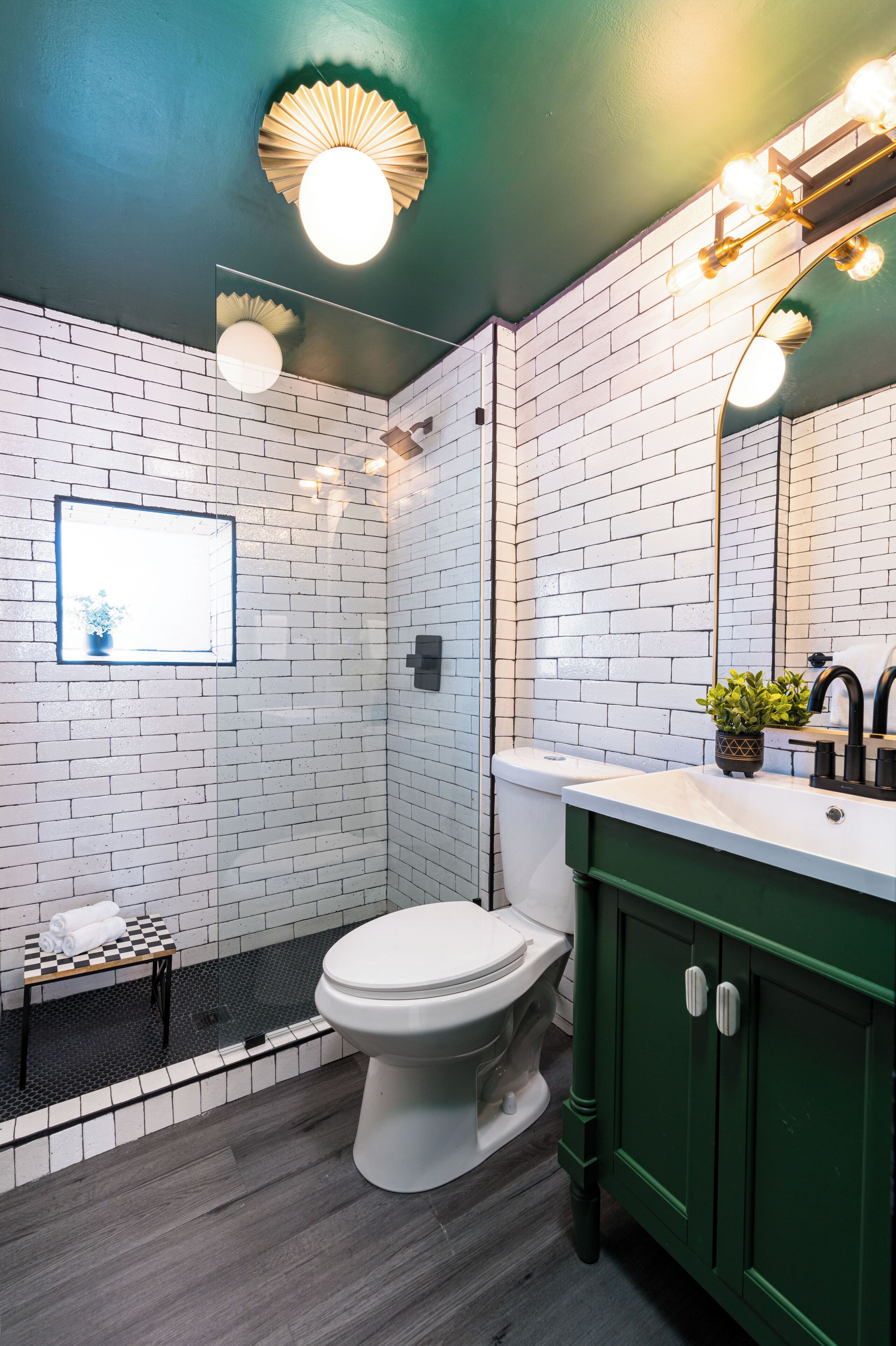 Et badeværelse med hvide murstensvægge, et hvidt toilet, en grøn kommode og et spejl med lys.