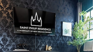 A modern living room with a flat-screen TV displaying a logo, a potted plant, books, and a decorative vase on a wooden coffee table. - Saint Philip French Quarter (New Orleans)