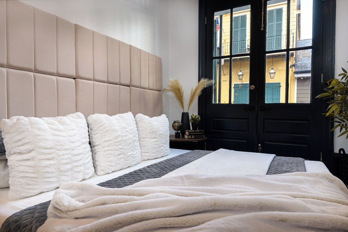 A bedroom with a large bed, a headboard, and a view of the street through a door.