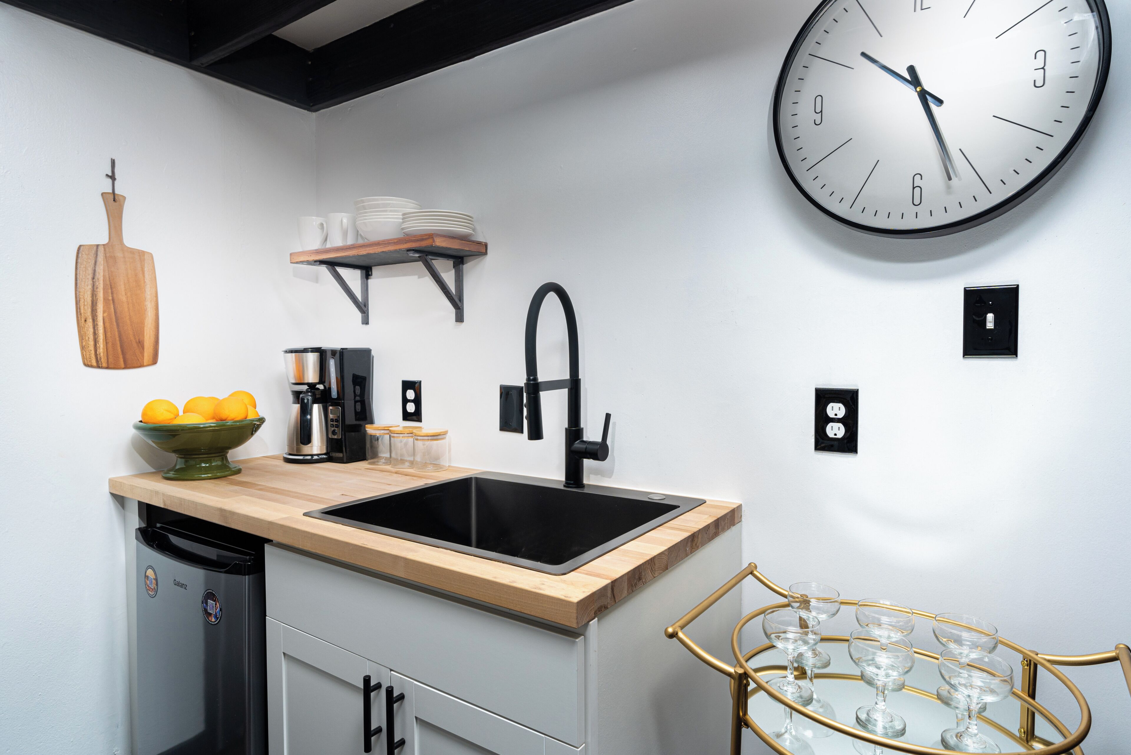 Een moderne keuken met een spoelbak, een koffieapparaat, een klok en een wijnglashouder.