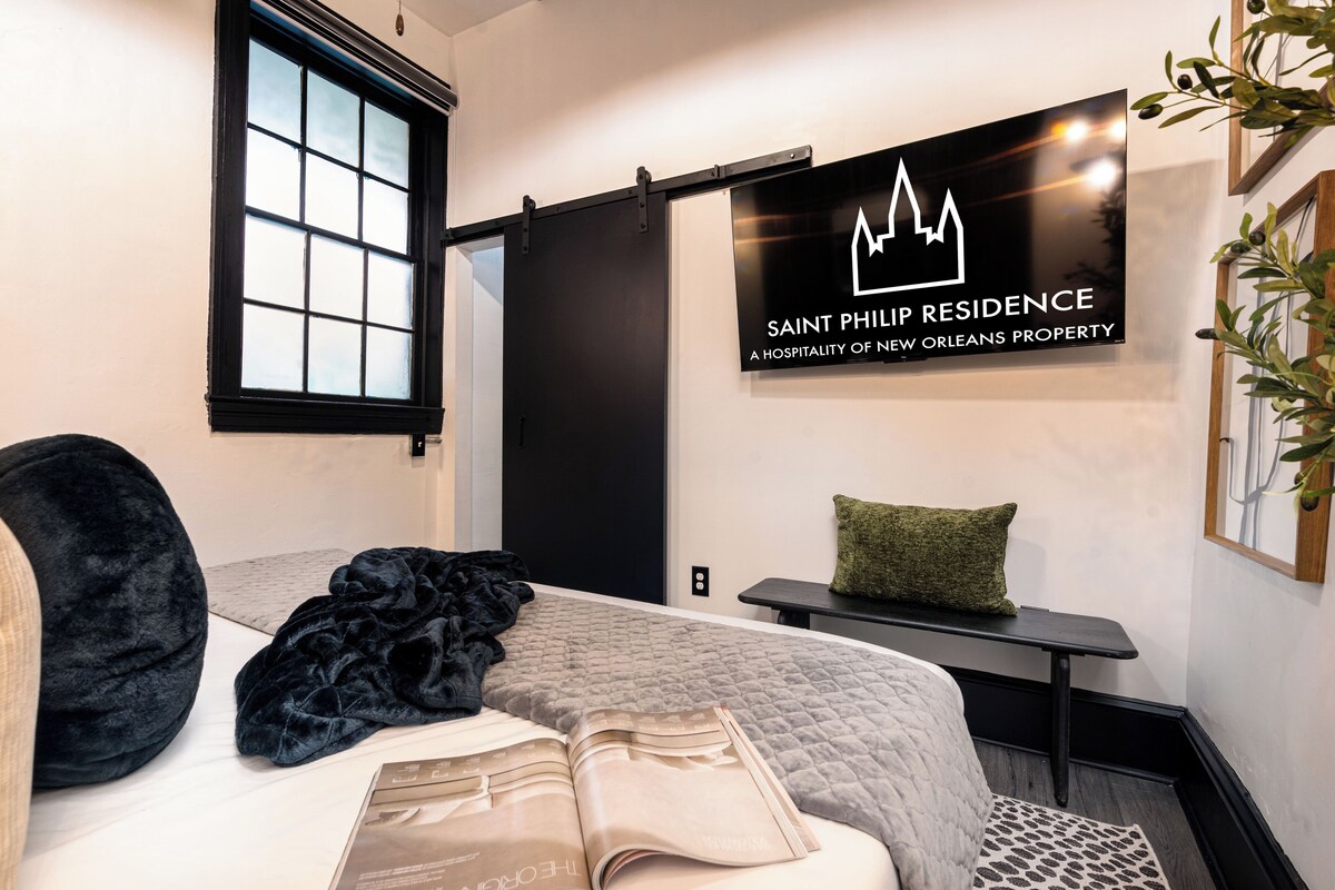 A hotel room with a bed, a bedside table, a window, and a wall-mounted sign.