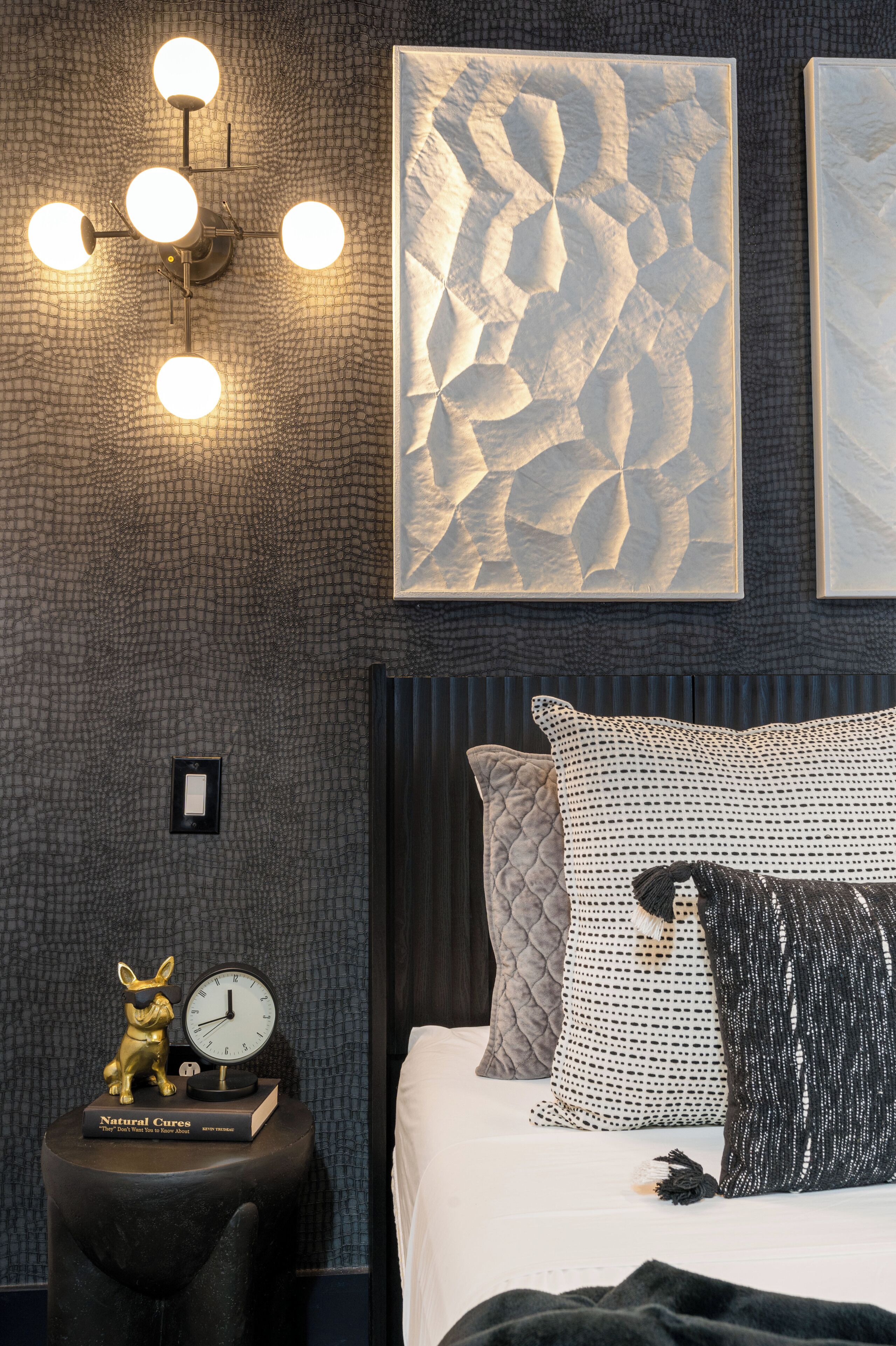 A bedroom with a bed, pillows, a clock, a nightstand, and a wall-mounted light fixture.