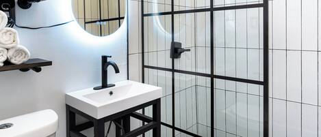 A modern bathroom with a glass shower enclosure, a white sink with a black faucet, and a toilet.