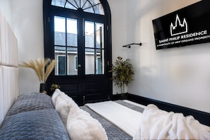 A hotel room with a large black door, a bed with grey and white bedding, a wall-mounted sign, and a potted plant. - Saint Philip French Quarter (New Orleans)