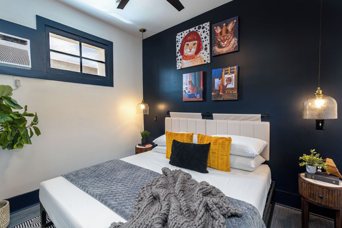 A modern bedroom with a bed, artwork on the wall, and a window.