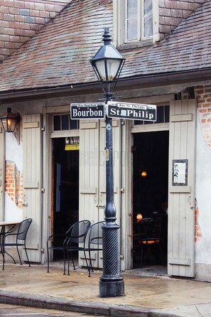 A street sign with Bourbon and St. Philip directions, a black lamp post, and a building entrance with a brick facade and wooden shutters. - Saint Philip Residence (New Orleans)