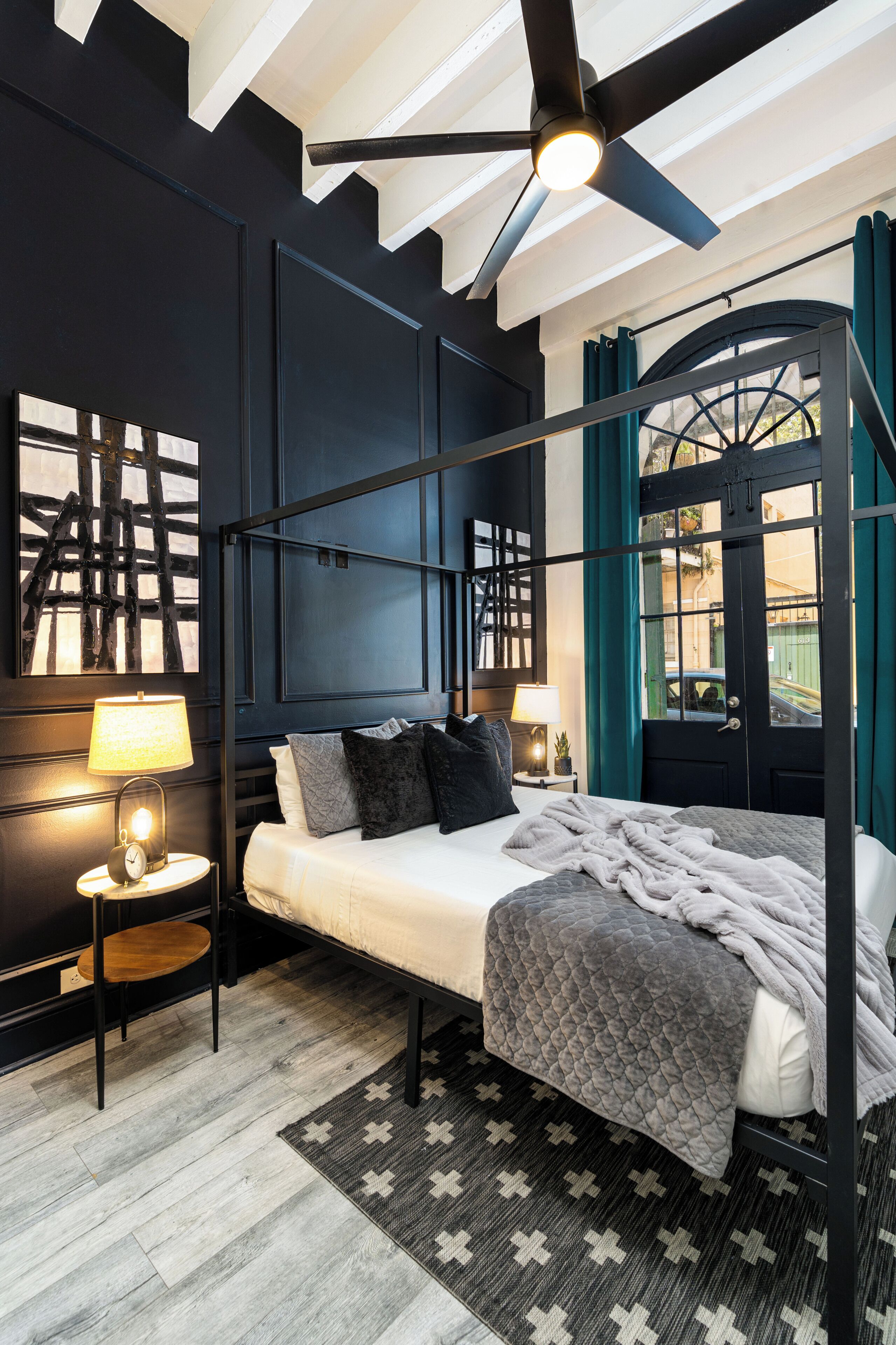A modern bedroom with a bed, bedside lamps, a ceiling fan, and a large window with curtains.